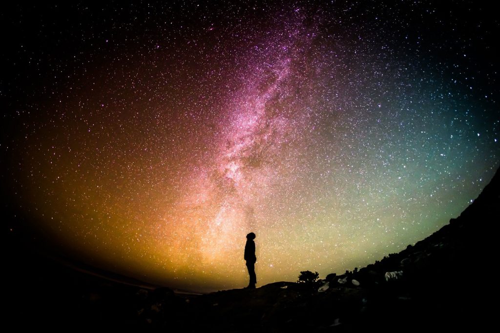 Silhouette of person standing looking up at colourful galaxy